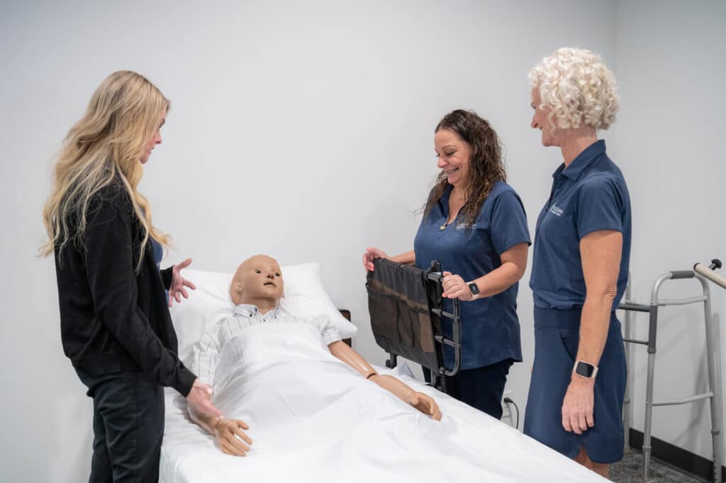 Caregiver receiving training with a mannequin on a bed, paying attention to the trainer.