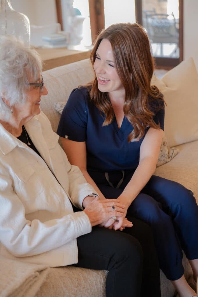 A caregiver and a senior are engaged in a warm conversation, both smiling at each other.