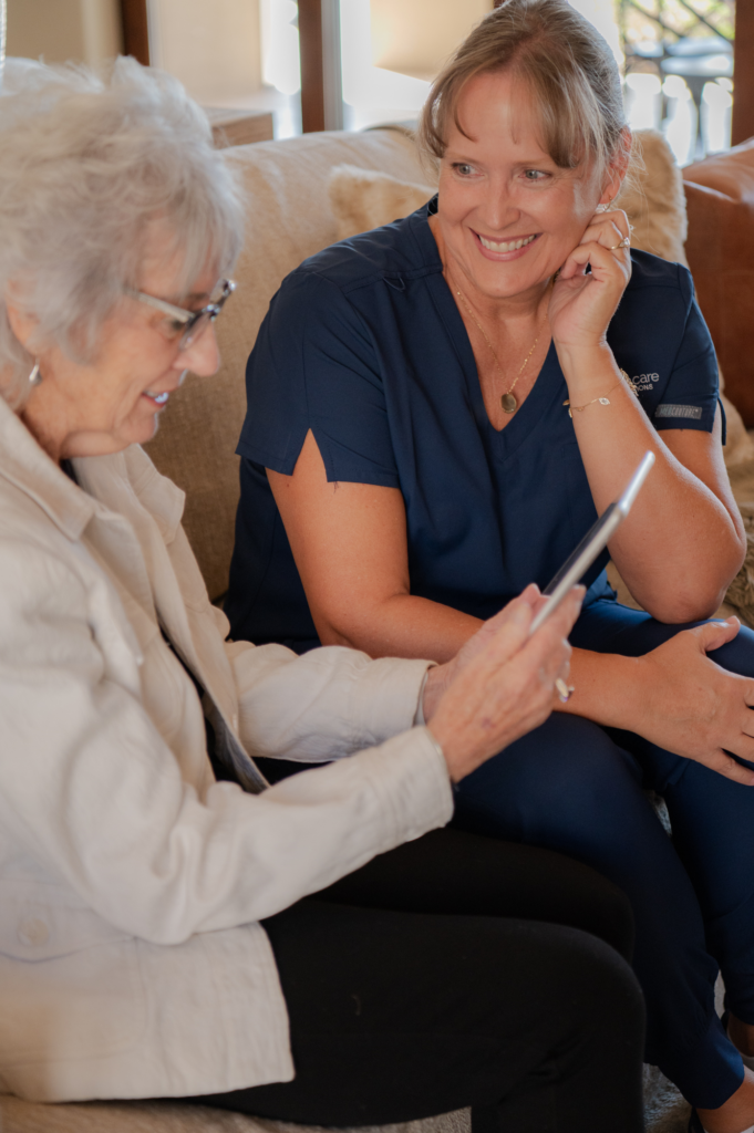 Caregiver listens attentively to a senior client who is smiling and looking at an iPad or tablet.